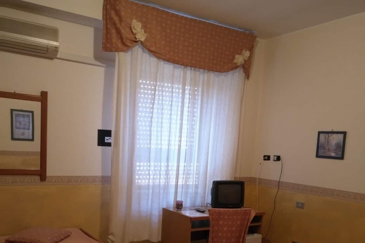 Une chambre d’hôtel avec deux lits, un bureau avec une télévision et une fenêtre avec des rideaux.