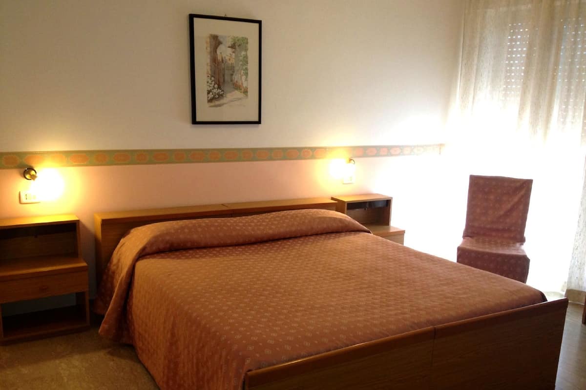 Une chambre d’hôtel avec un lit en bois, deux tables de chevet, une chaise et un tableau encadré au mur.