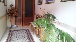A hallway with a wooden door, a potted plant, a patterned rug, and framed pictures on the wall. - Diavin (Vibo Valentia)