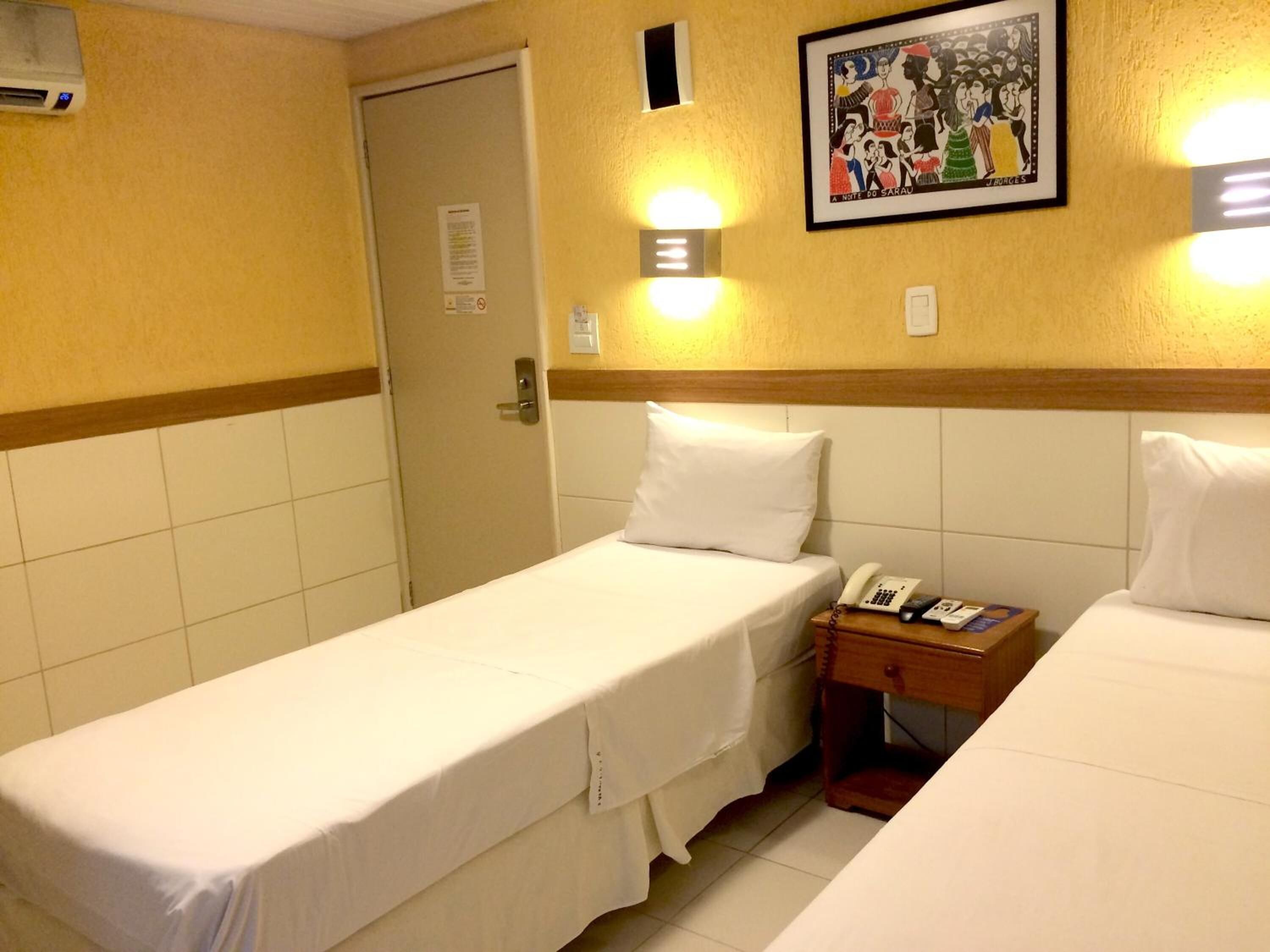 Habitación de hotel con dos camas individuales, una mesita de noche con teléfono y una lámpara fijada a la pared.