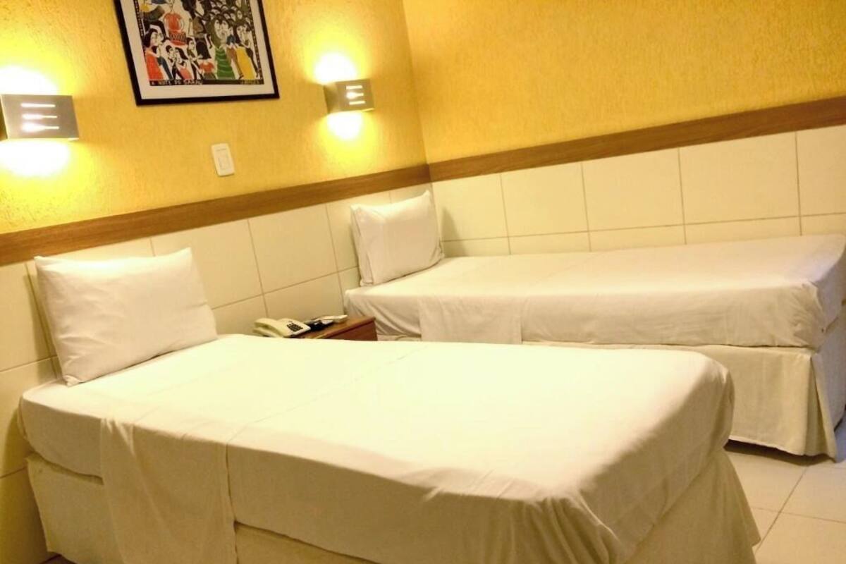 Duas camas de solteiro em um quarto com parede azulejada e quadro pendurado acima das camas.