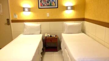 A hotel room with two single beds, a small bedside table, a nightstand, a telephone, and a framed picture on the wall.
