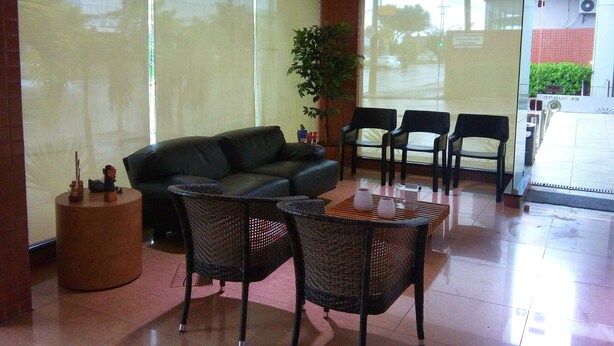A reception area with a black leather sofa, wicker chairs, a small round table, and a potted plant. - Hotel Veraneio (Recife)