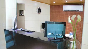 A reception desk with a computer monitor, a clock, and an air conditioning unit. - Hotel Veraneio (Recife)