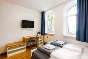 A hotel room with a wooden desk, a chair, two beds, a flat-screen TV, and a window with curtains. - mk | bed & breakfast münchen (Munich)