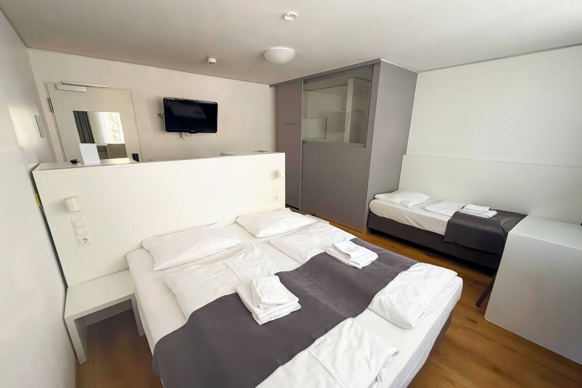 A modern hotel room with a large bed, a smaller sofa, a TV, and a mirror.