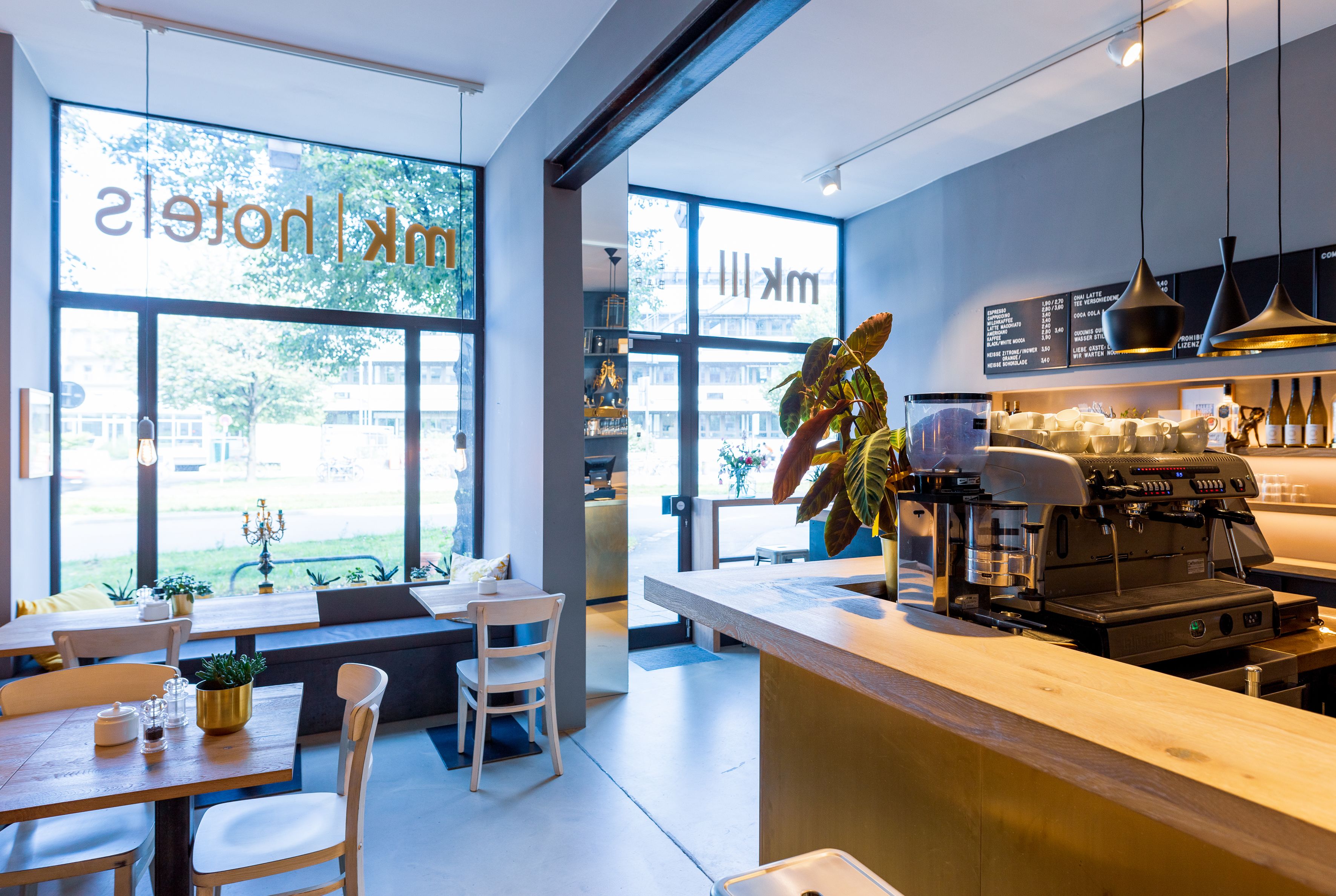 Un café moderne avec un décor contemporain, un bar, des espaces pour s’asseoir et de grandes fenêtres donnant sur l’extérieur.