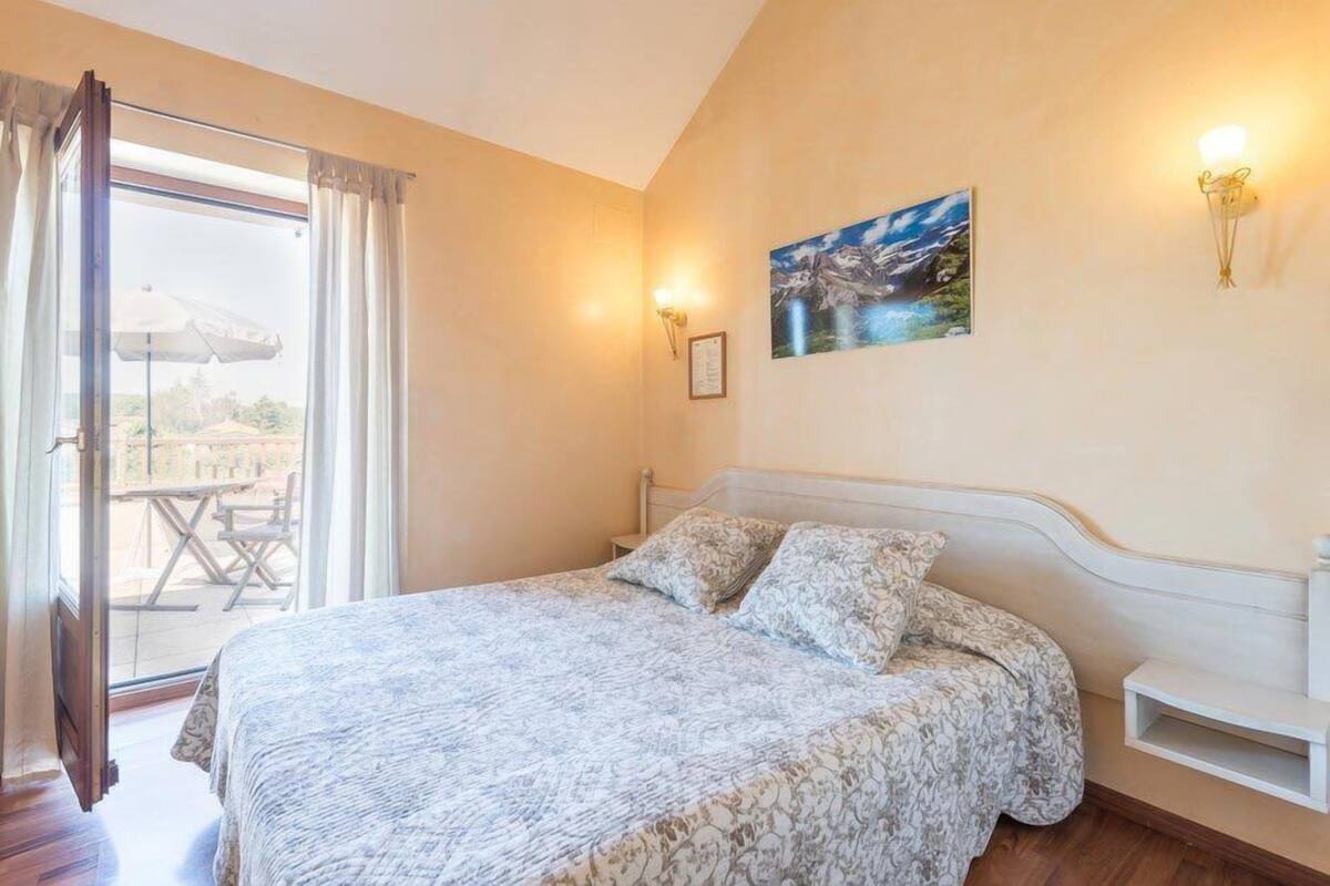 A bedroom with a bed, a painting on the wall, and a window with curtains.