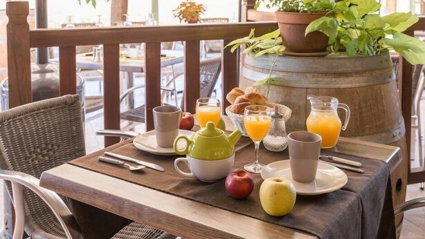 A breakfast table set with a teapot, cups, a jug of orange juice, a pitcher, and fresh fruits.
