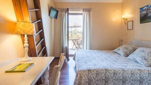 A bedroom with a bed, a desk, a chair, a TV, and a window with curtains.