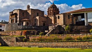 Edifici de pedra històric amb una torre campanar destacada i una cúpula gran, envoltat d'un jardí ben cuidat i una muralla de pedra.