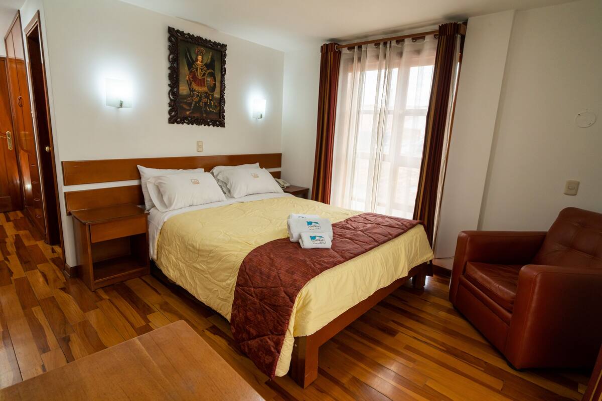Ein Hotelzimmer mit einem hölzernen Bett, einem braunen Ledersessel, einem Nachttisch aus Holz und einem Bild an der Wand.