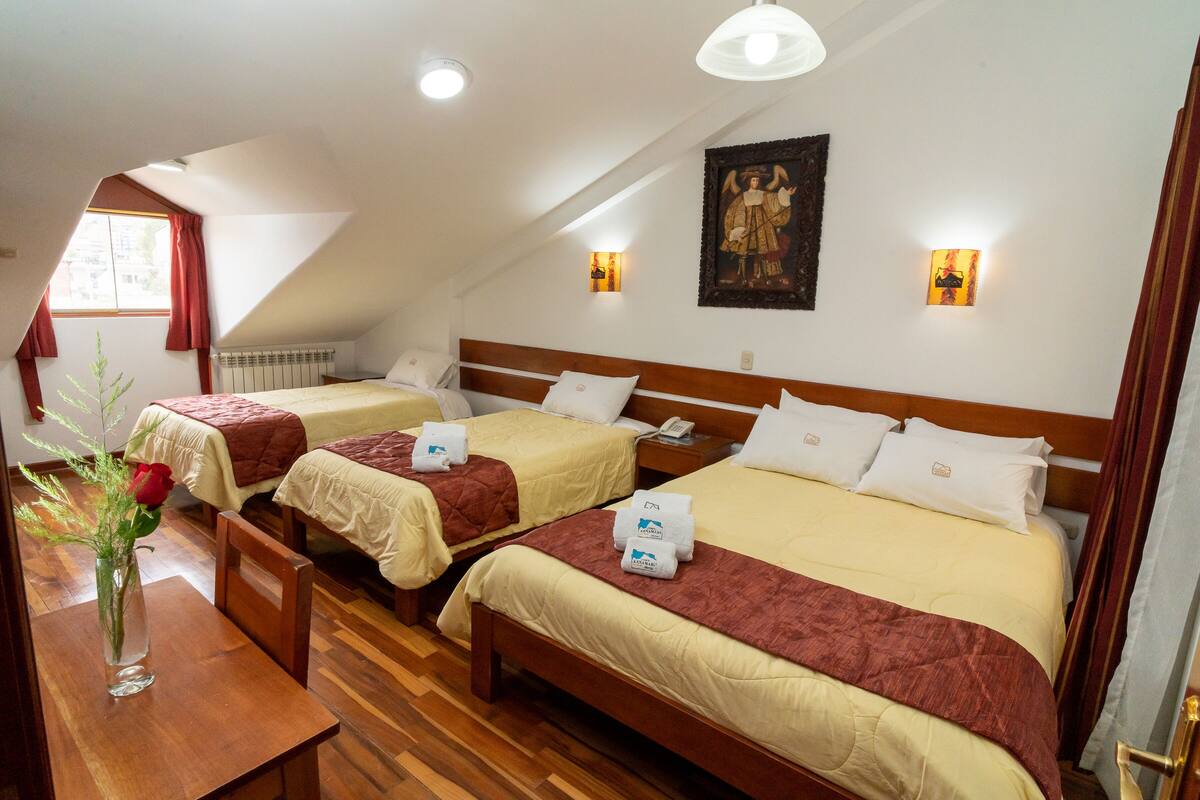 Ein Hotelzimmer mit zwei Einzelbetten, einem Holzkopfteil, einer Vase mit einer Rose und einem Bild an der Wand.
