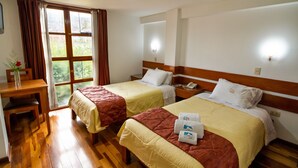 Habitació d'hotel amb dos llits, sòl de fusta, escriptori i finestra amb cortines.