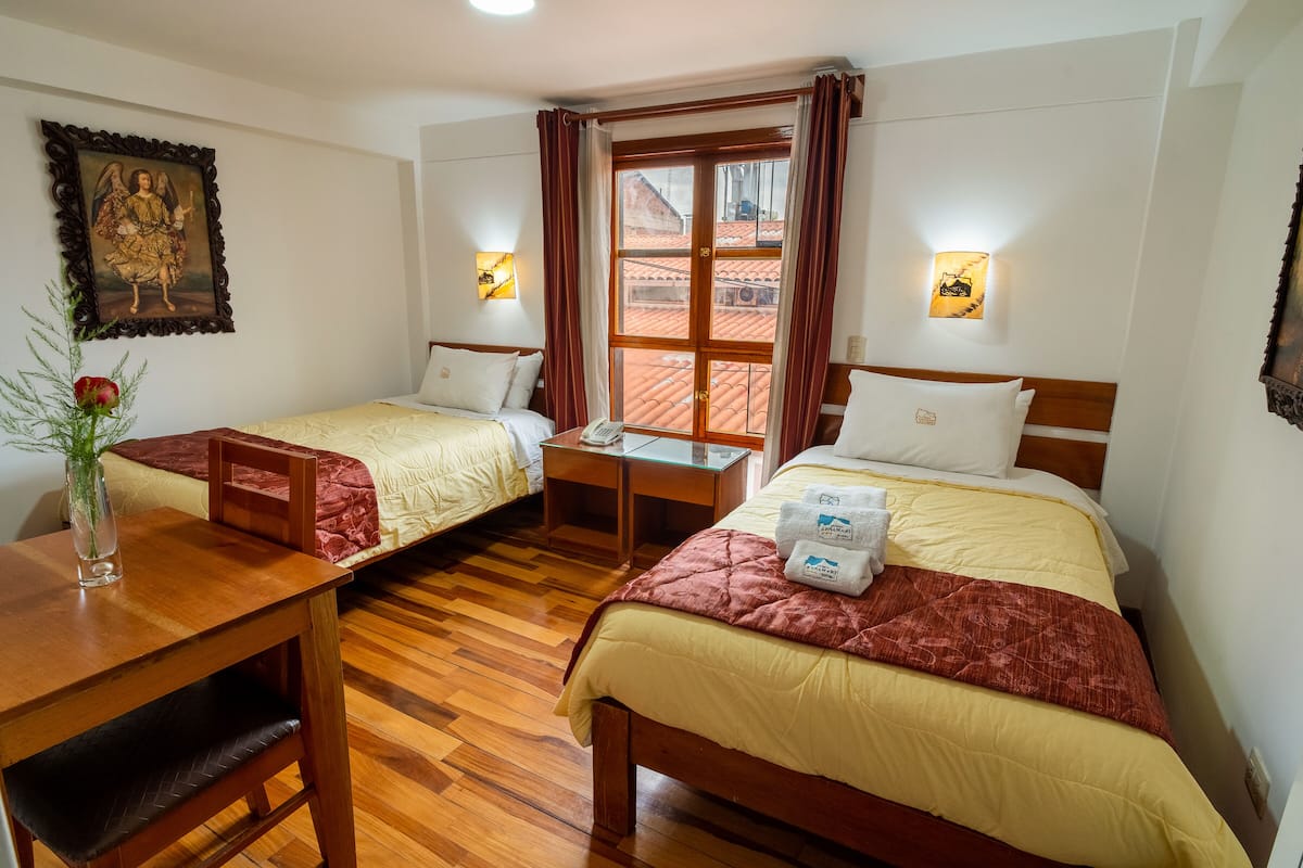 Ein Hotelzimmer mit zwei Betten, Holzboden, einem Tisch mit einer Vase und einem Bild an der Wand.