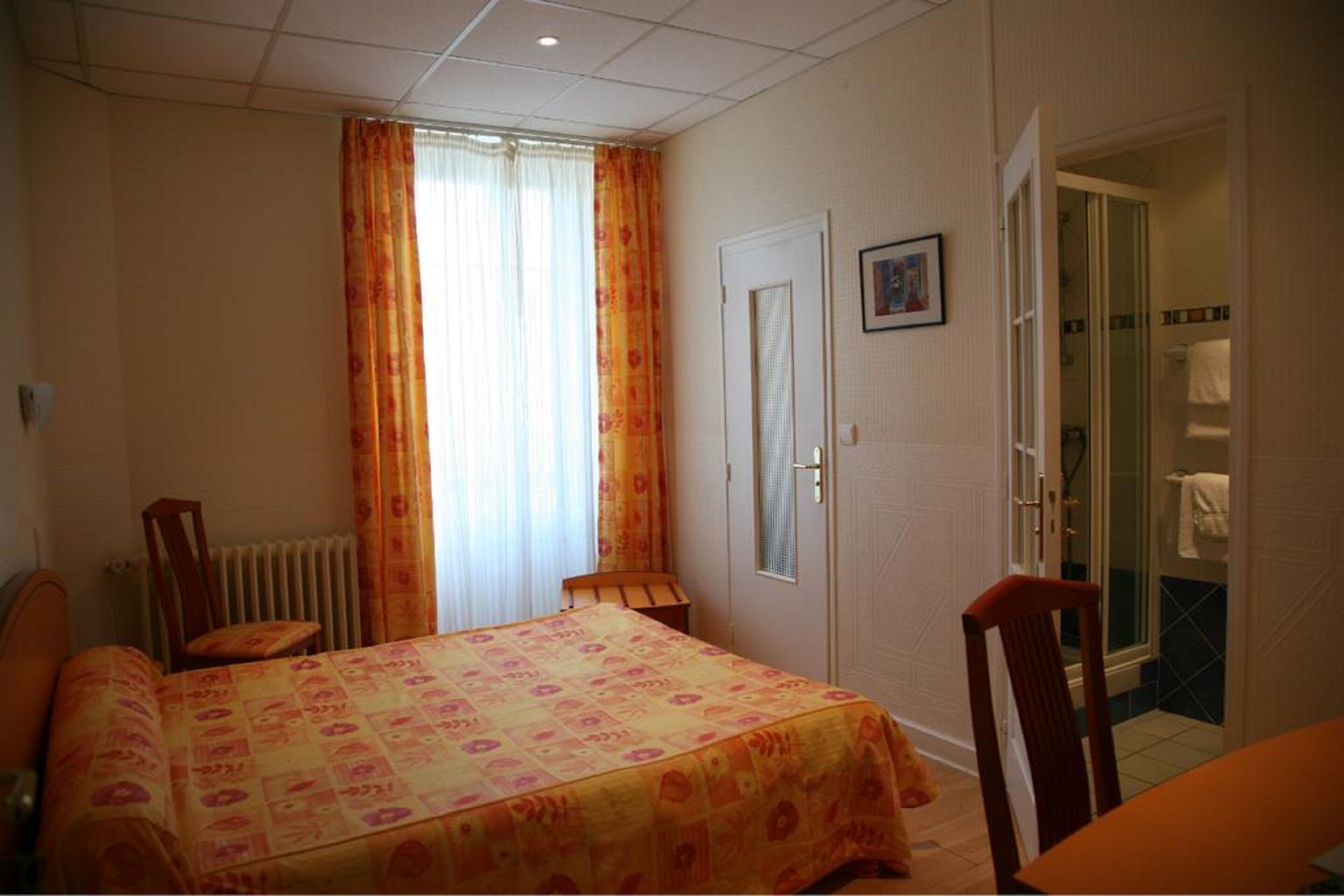 Un dormitorio con cama, una silla, un radiador, una puerta y un baño visible a través de una puerta abierta.