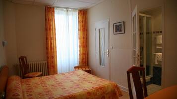 A bedroom with a bed, a chair, a radiator, a door, and a bathroom visible through an open door.