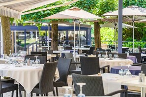 An outdoor dining area with tables and chairs, covered by umbrellas, and surrounded by greenery. - Hotel Le Sablier Du Temps (Argentat-sur-Dordogne)