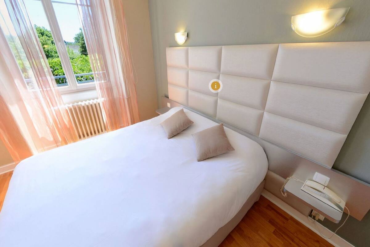 A modern bedroom with a large bed, two bedside lamps, and a view of greenery outside.