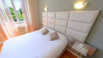 A modern bedroom with a large bed, two bedside lamps, and a view of greenery outside.