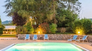 Un área de piscina con sillones, una zona de estar cubierta y una pared de piedra.