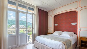 Habitación de hotel con una cama grande, vistas a la ciudad y un balcón con puerta corredera.