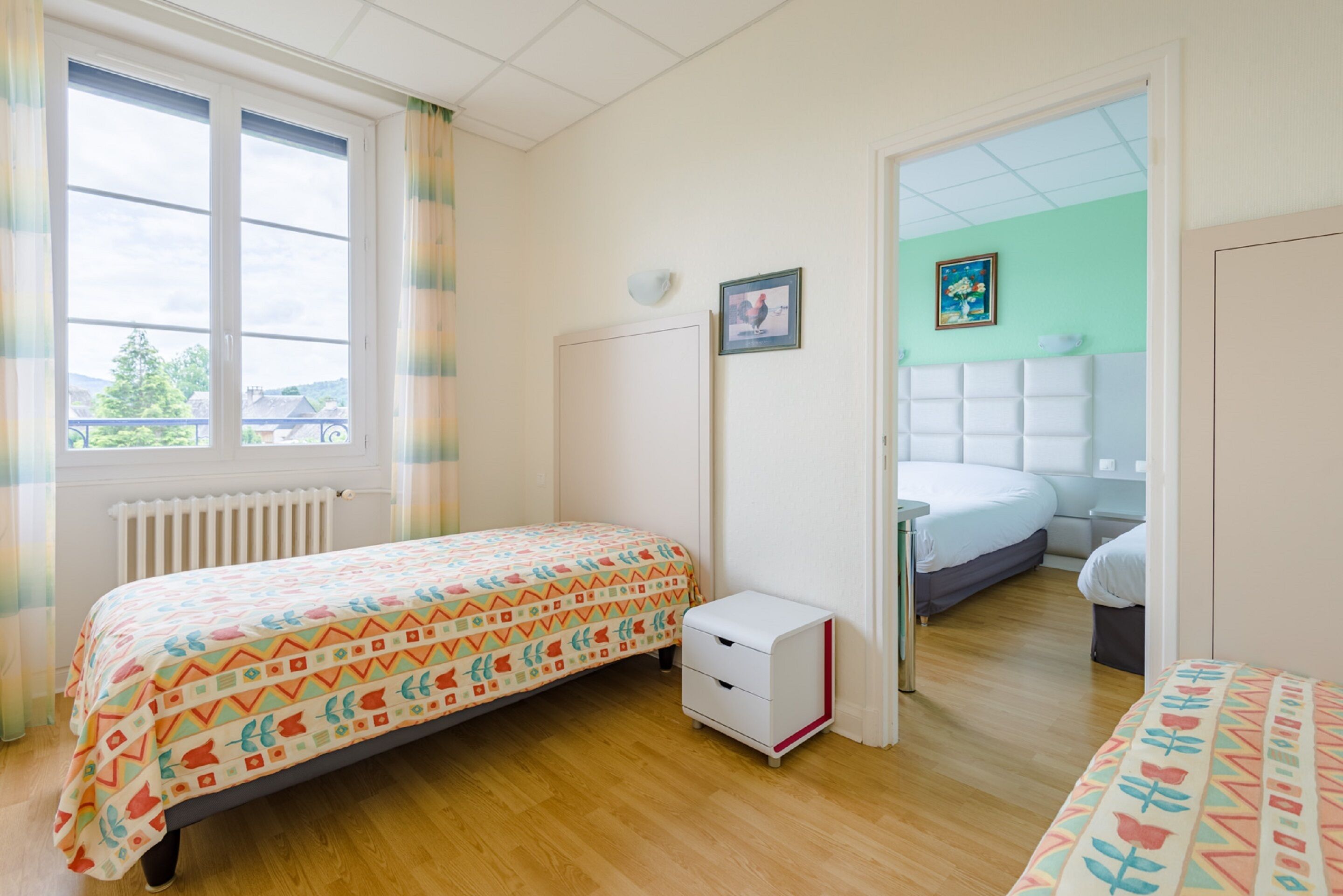 Une chambre à coucher avec un lit, une table de chevet, un radiateur et une fenêtre avec des rideaux.
