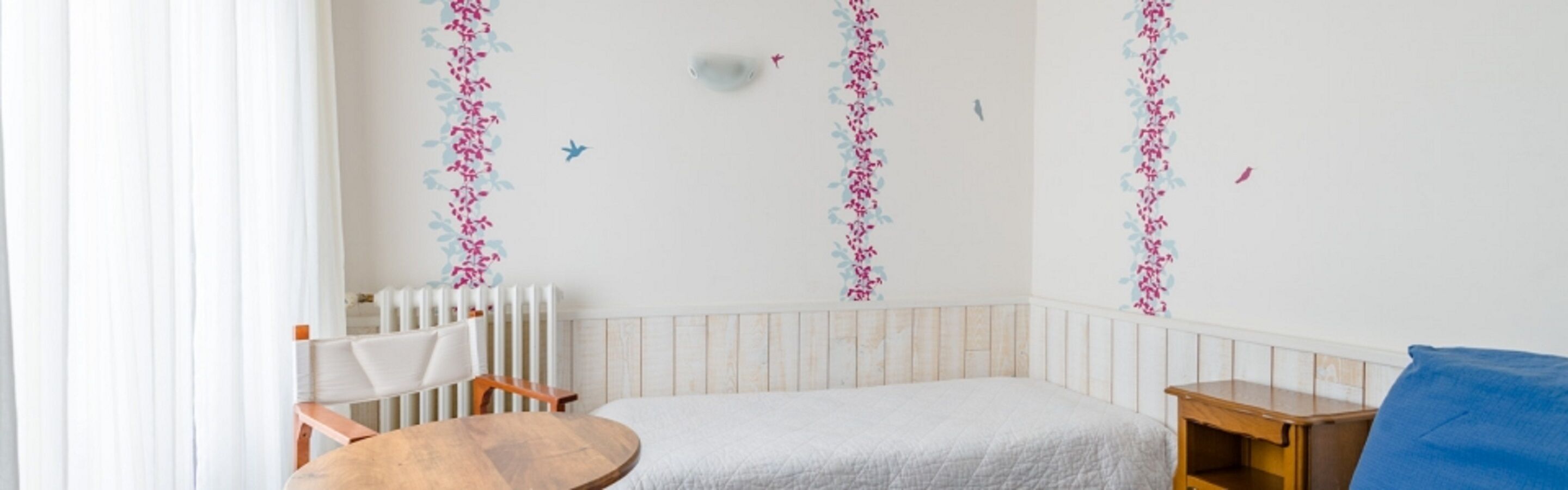 Een kinderkamer met een ledikant, een klein rond tafeltje en een blauw kussen.