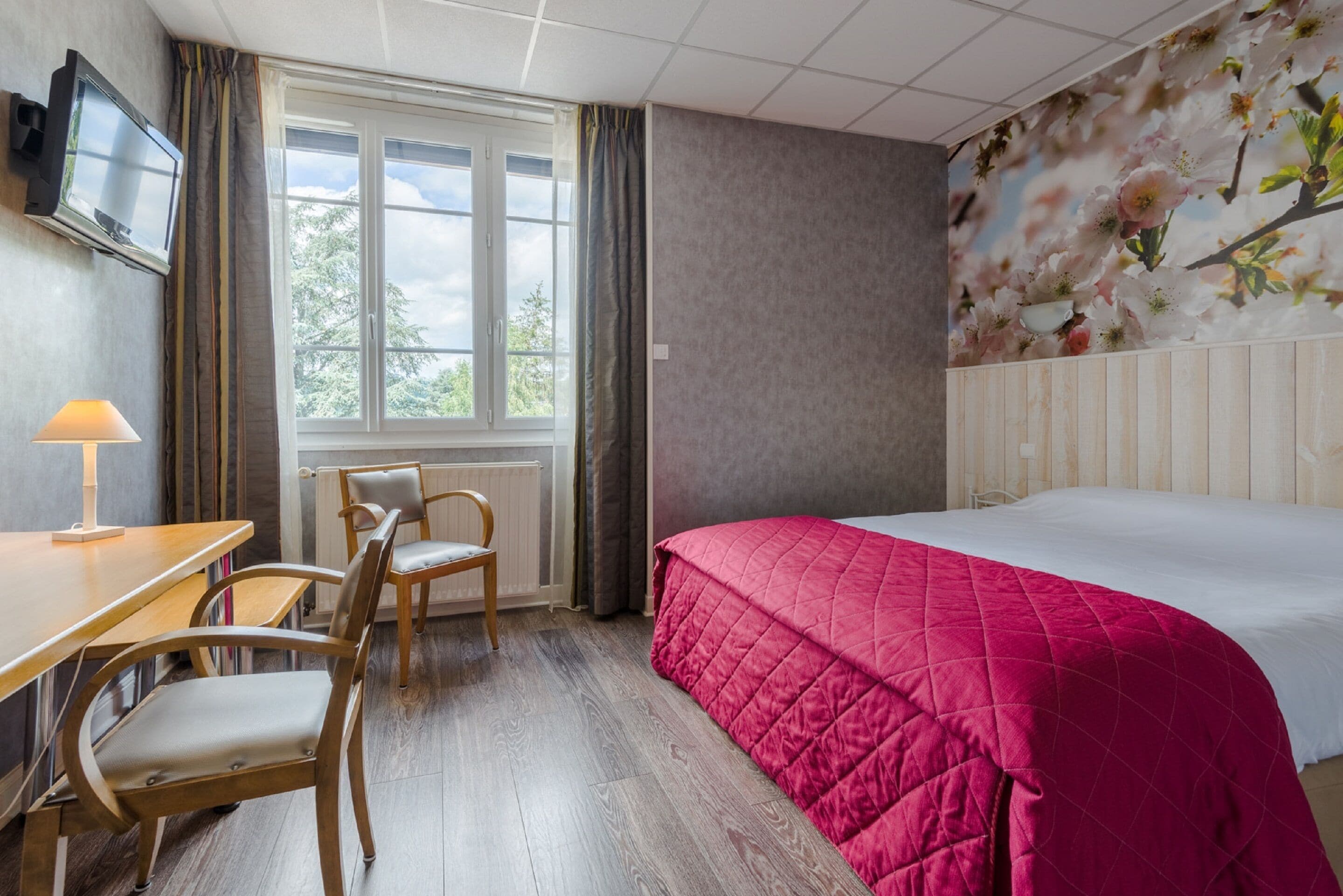 Habitación de hotel con cama, escritorio con silla, televisor y ventana con cortinas.
