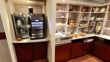 A kitchenette with a coffee machine, shelves with kitchenware, and a small sink.