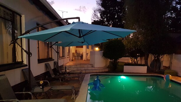 Una piscina con una sombrilla azul, sillas de descanso y un patio con una mesa y sillas.