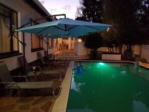 Una piscina con una sombrilla azul, sillas de descanso y un patio con una mesa y sillas.