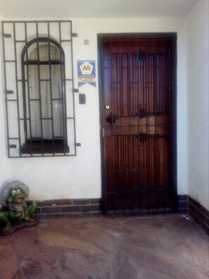 Una puerta de madera con una verja metálica, una ventana con barrotes y un cartel que indica 'AA Quality Assured'.