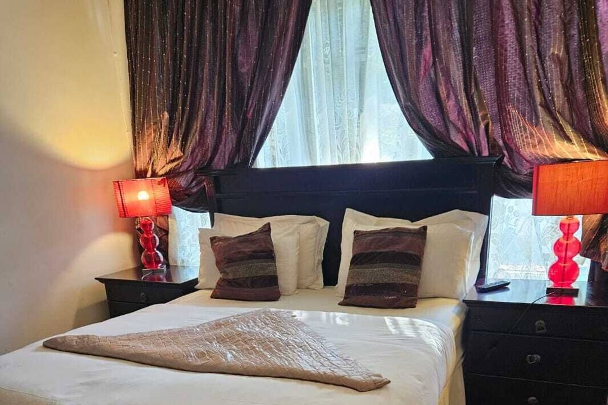 A neatly made bed with a white comforter and a brown throw blanket, a dark wooden headboard, and a red patterned rug on the floor.