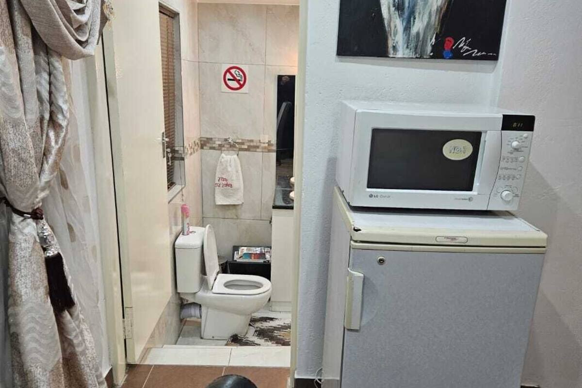 A compact living space with a microwave on a small fridge, a toilet, and a shower area.