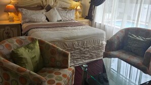 Un dormitorio con una cama grande, dos sillones, una mesa de centro de vidrio y una ventana con cortinas.