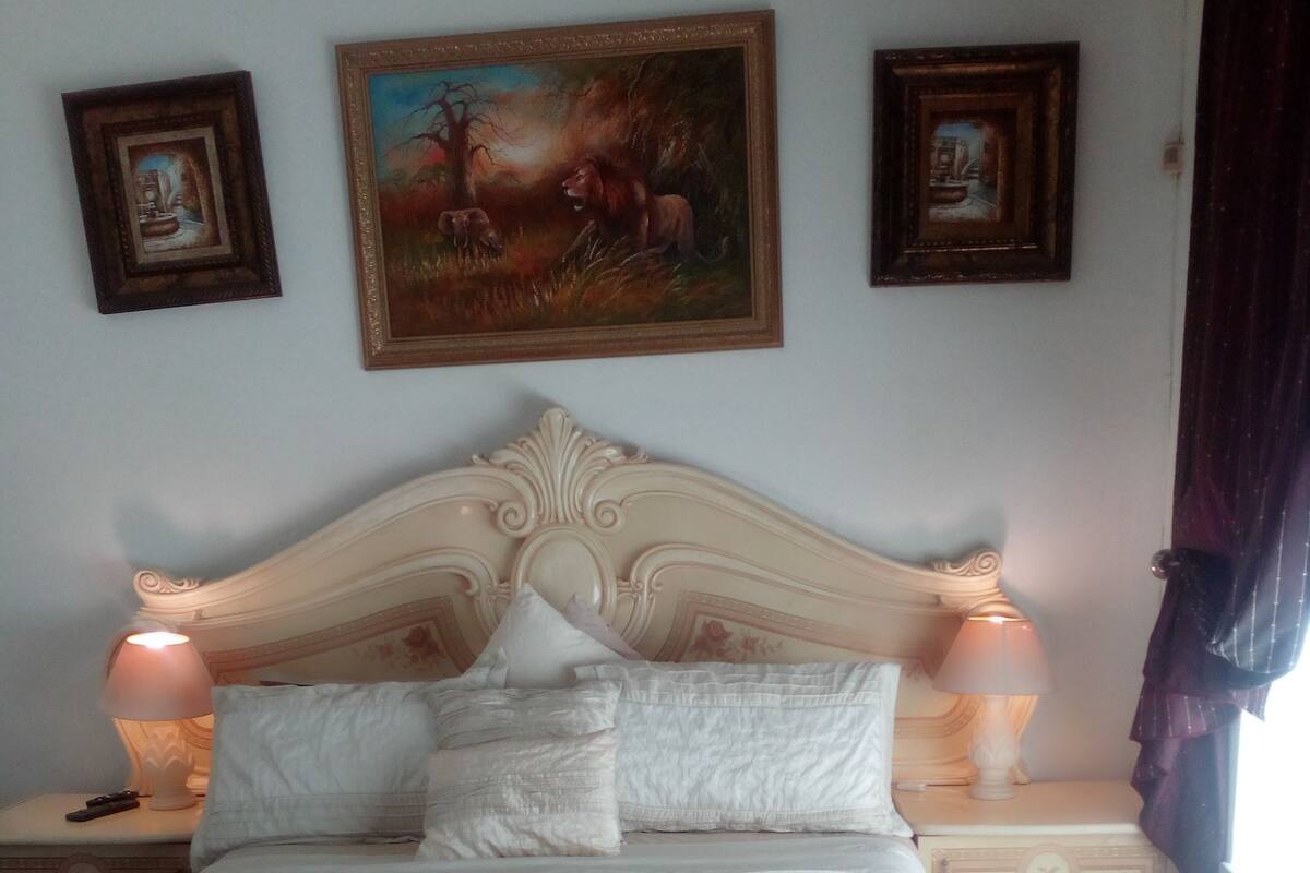 A neatly made bed with white linens, two bedside lamps, and a floral-patterned chair.