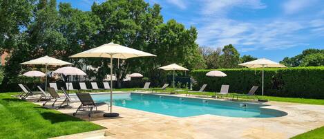 A swimming pool with lounge chairs and umbrellas, surrounded by a well-maintained lawn and hedges.