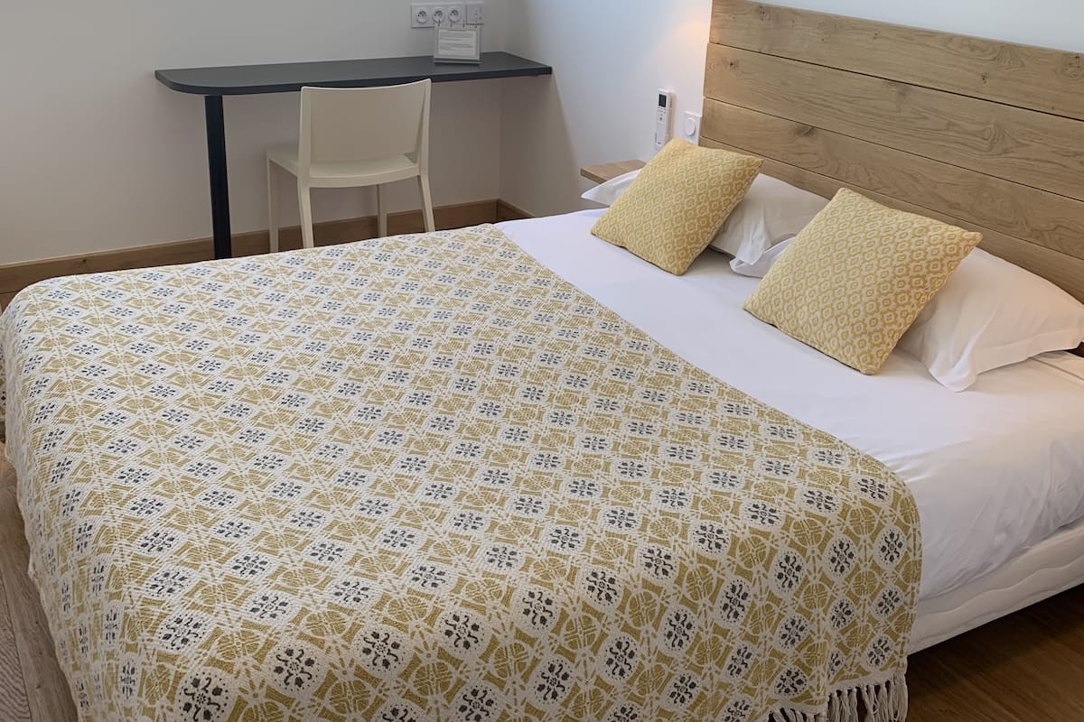 A bedroom with a bed, bedside table, lamp, and a desk with a chair.