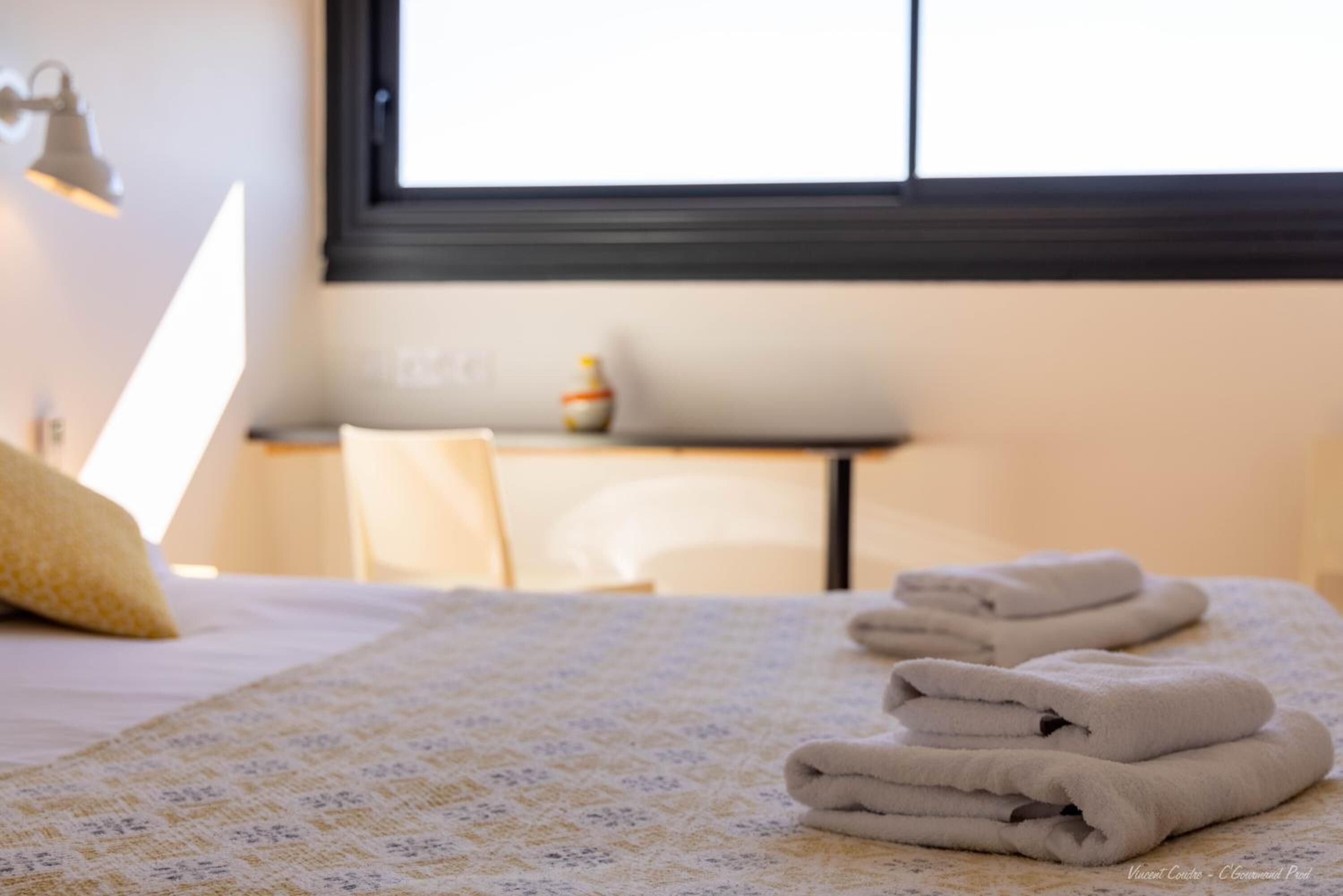 A neatly made bed with folded towels, a bedside lamp, and a small table with a vase.