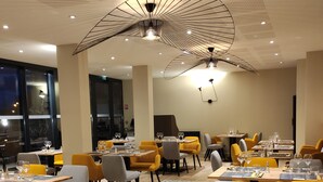 A modern dining area with yellow and grey chairs, wooden tables, and a unique ceiling design. - Hotel Bellaroc (Rocamadour)