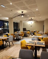 Un comedor moderno con sillas amarillas y grises, mesas de madera y un diseño de techo único.