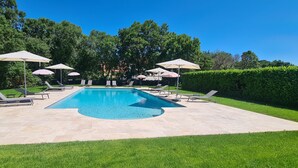 A swimming pool with lounge chairs and umbrellas, surrounded by well-maintained grass and trees. - Hotel Bellaroc (Rocamadour)