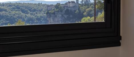 A room with a window overlooking a cityscape, a small table with a vase, and a chair.
