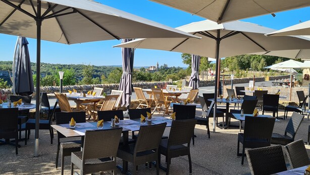 An outdoor dining area with tables and chairs under umbrellas, overlooking a scenic landscape. - Hotel Bellaroc (Rocamadour)