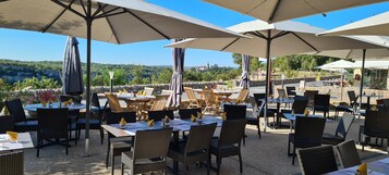 Un área de comedor al aire libre con mesas y sillas bajo sombrillas, con vistas a un paisaje pintoresco.