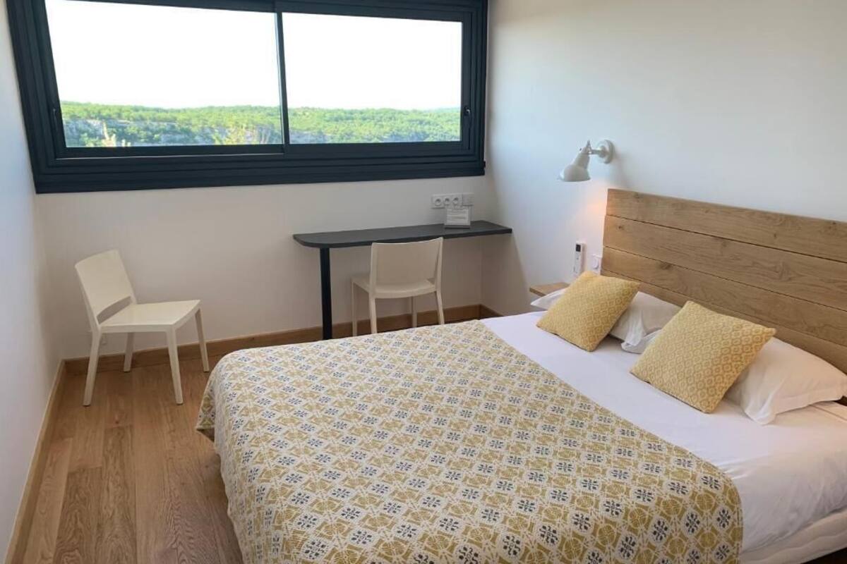 A bedroom with a bed, two chairs, a desk, and a window with a view.