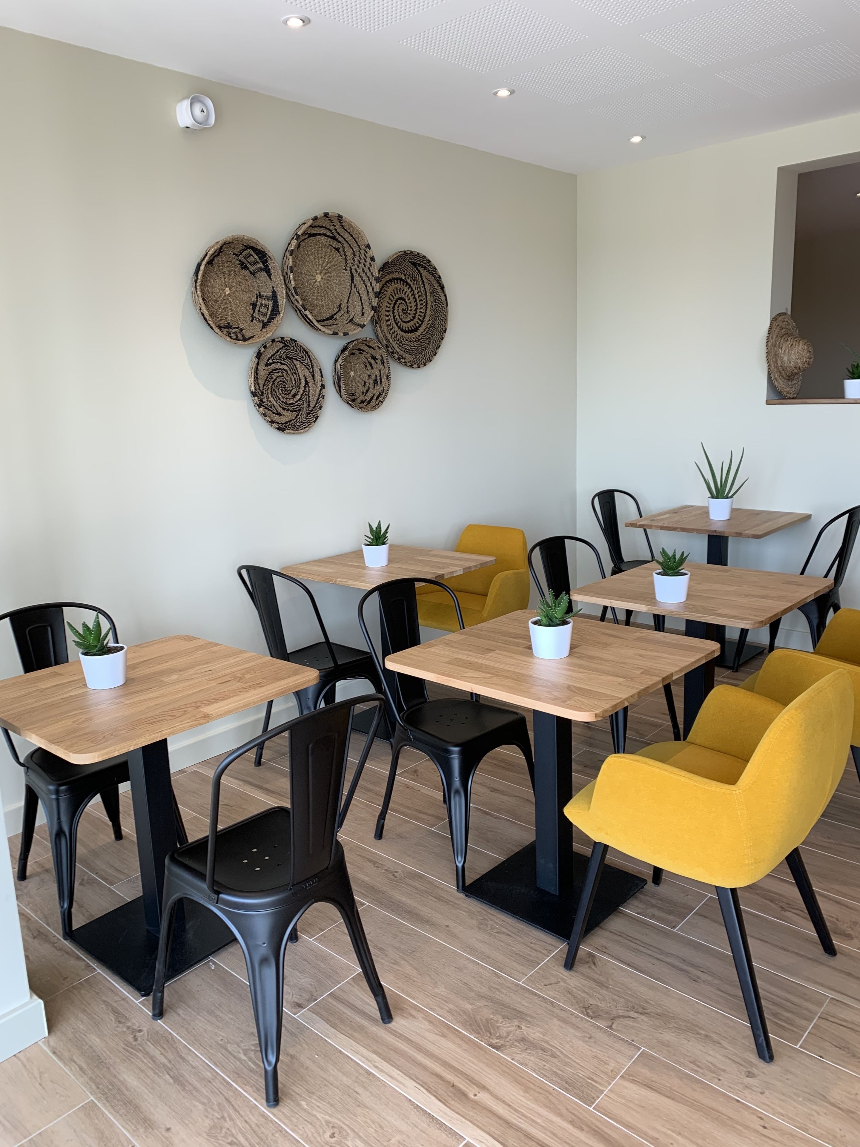 Un espace repas moderne avec des tables en bois, des chaises noires et jaunes, et des œuvres d’art décoratives sur les murs.