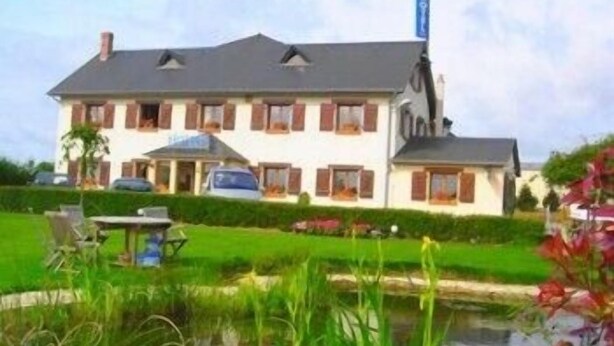 Een huis met twee verdiepingen, een schuin dak, een zichtbare schoorsteen en een kleine tuin met een vijver.