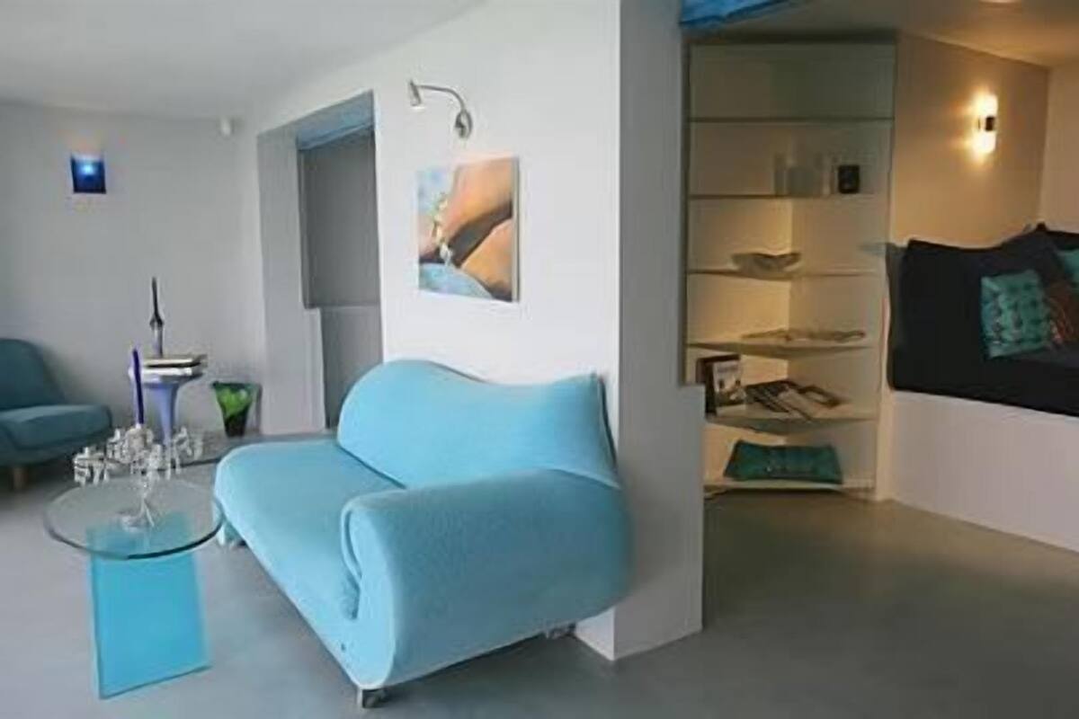 A modern living room with a blue sofa, a glass coffee table, and a wall-mounted shelf with decorative items.